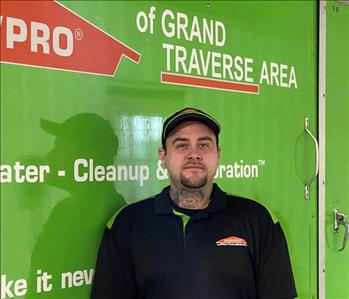 Male brown haired wearing hat standing in front of green SERVPRO vehicle
